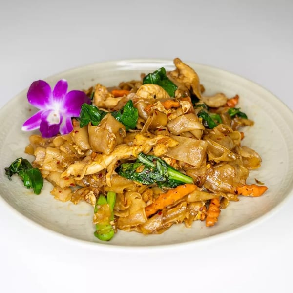 Pad See Ew with chicken and vegetables, garnished with a purple orchid on a white plate.