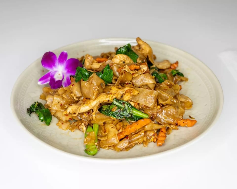 Pad See Ew with chicken and vegetables, garnished with a purple orchid on a white plate.