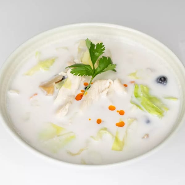 Creamy white soup with chicken, cabbage, mushrooms, and red oil drops, garnished with cilantro.