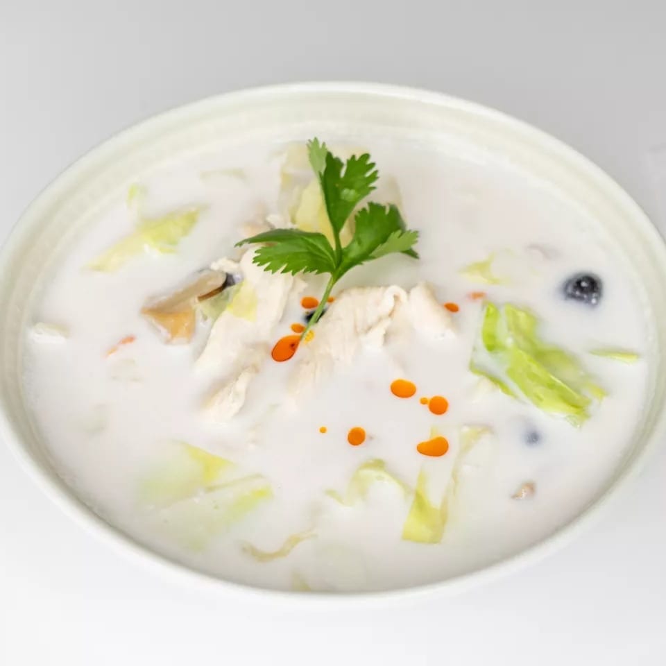 Creamy white soup with chicken, cabbage, mushrooms, and red oil drops, garnished with cilantro.