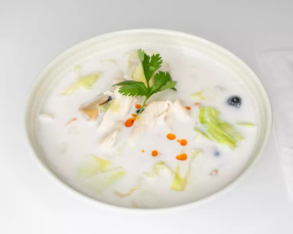 Creamy white soup with chicken, cabbage, mushrooms, and red oil drops, garnished with cilantro.
