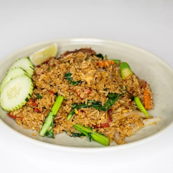 Fried rice with vegetables, meat, and a lime wedge, served on a light-colored plate.