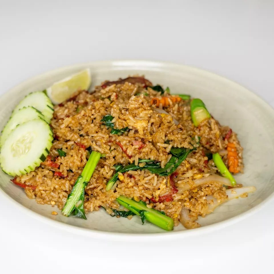 Fried rice with vegetables, meat, and a lime wedge, served on a light-colored plate.
