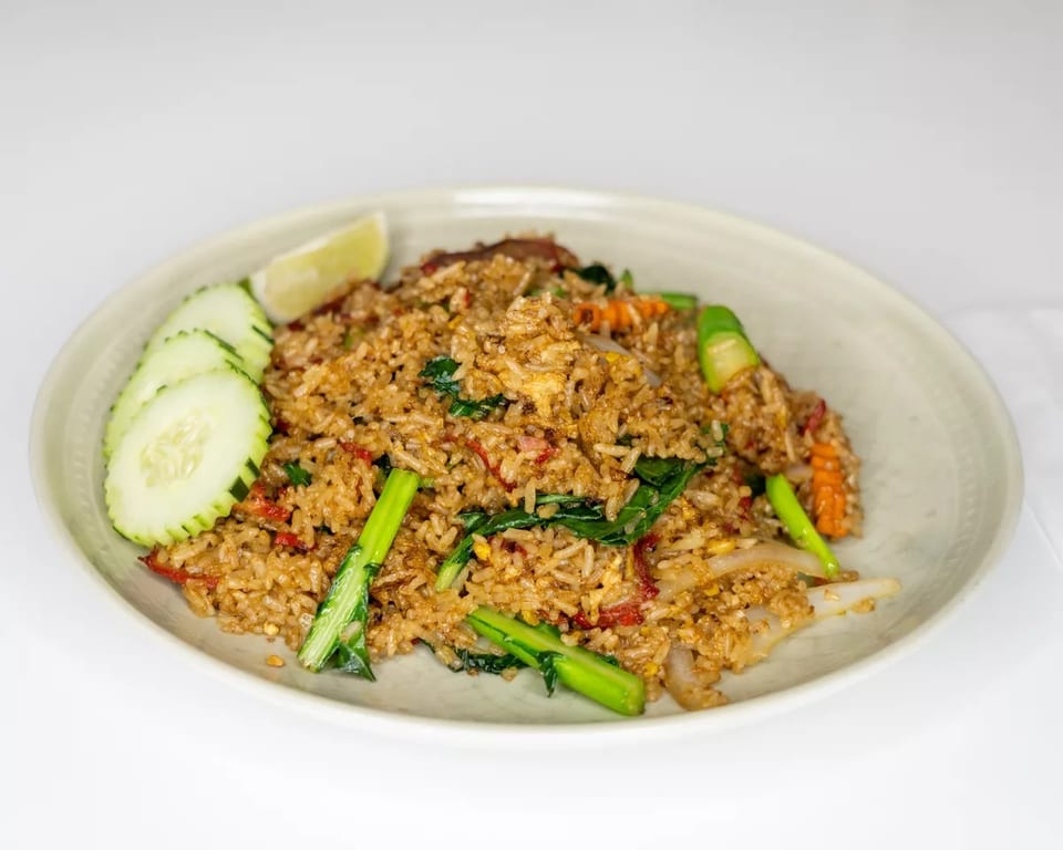 Fried rice with vegetables, meat, and a lime wedge, served on a light-colored plate.