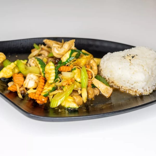 Stir-fried vegetables with chicken and white rice on a black rectangular plate.
