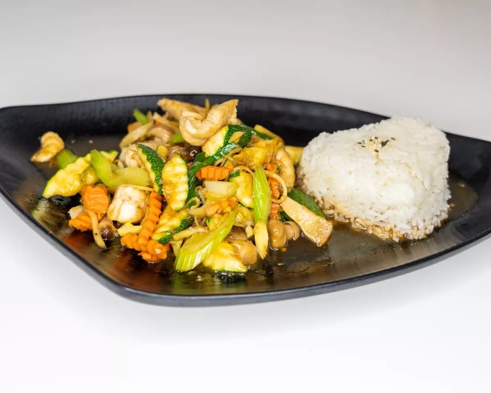 Stir-fried vegetables with chicken and white rice on a black rectangular plate.