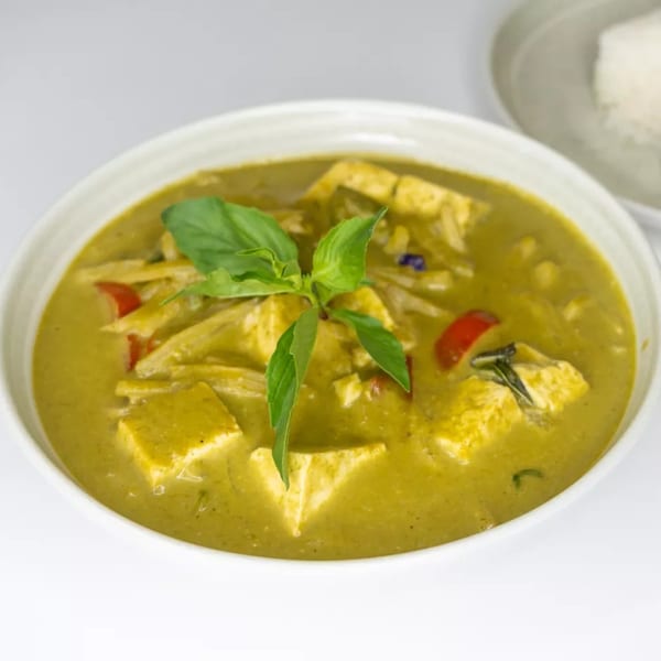 Green curry with tofu, bamboo shoots, and red peppers, garnished with basil, served with rice.