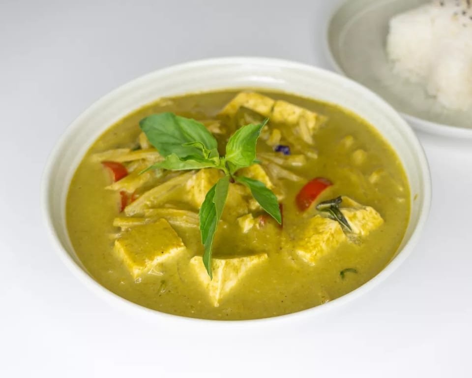 Green curry with tofu, bamboo shoots, and red peppers, garnished with basil, served with rice.