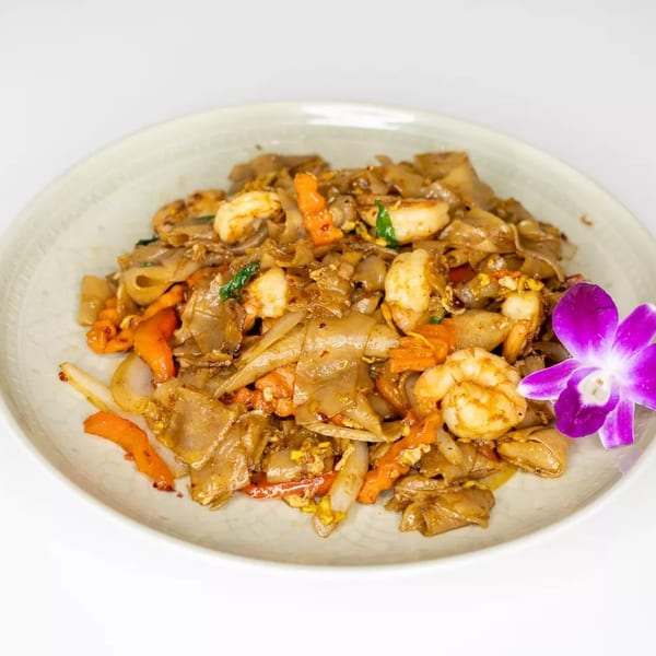 Pad See Ew with shrimp, carrots, and onions, garnished with a purple orchid.