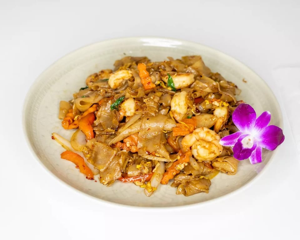 Pad See Ew with shrimp, carrots, and onions, garnished with a purple orchid.