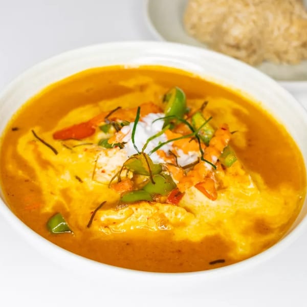 A white bowl of yellow curry with green and orange vegetables, topped with coconut cream.