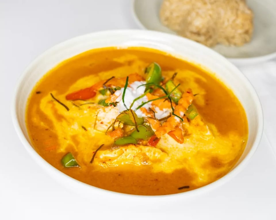 A white bowl of yellow curry with green and orange vegetables, topped with coconut cream.