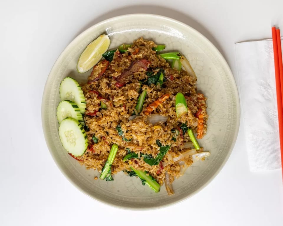 Fried rice with vegetables, meat, cucumber slices, and a lime wedge on a plate with chopsticks.
