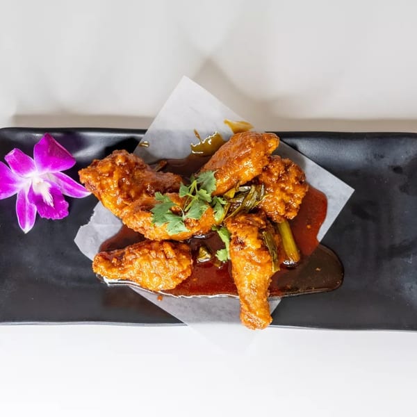 Crispy chicken wings with a sweet and spicy sauce, garnished with cilantro and a purple orchid.