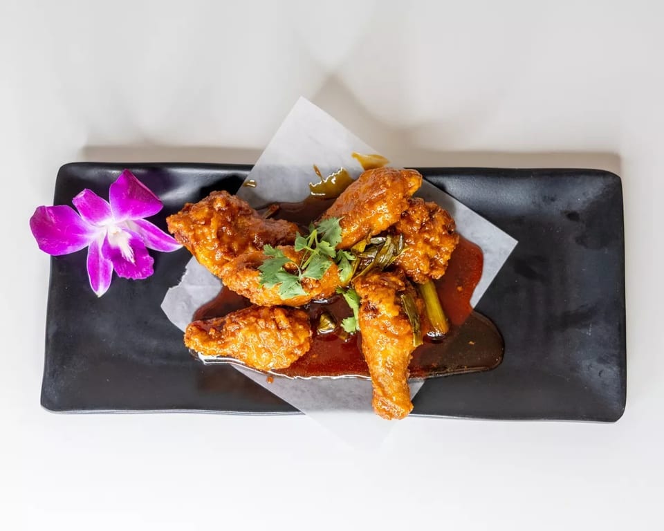 Crispy chicken wings with a sweet and spicy sauce, garnished with cilantro and a purple orchid.