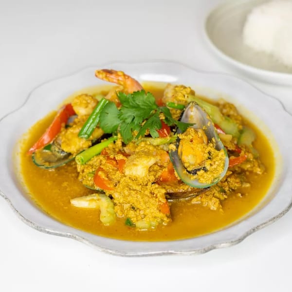 Seafood curry with mussels, shrimp, and vegetables in a yellow sauce, served with rice.
