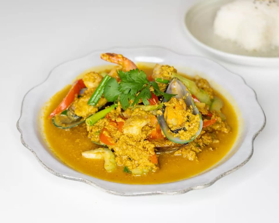 Curry seafood dish with mussels, shrimp, and vegetables in a yellow sauce, with rice in the background.