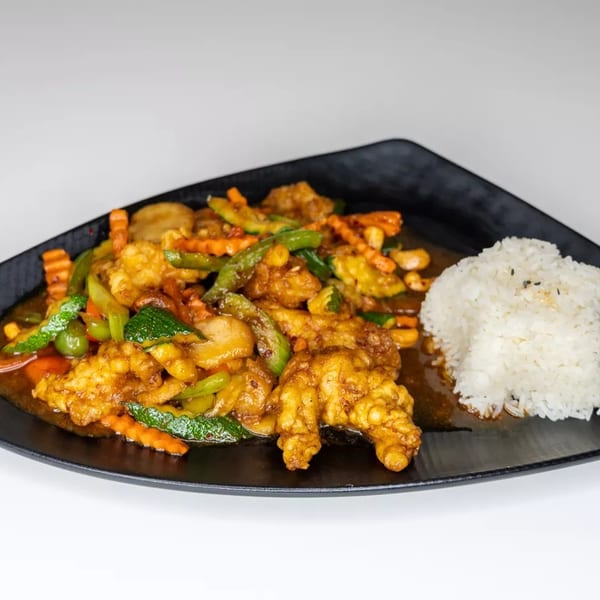 Crispy chicken stir-fry with colorful vegetables and white rice on a black plate.