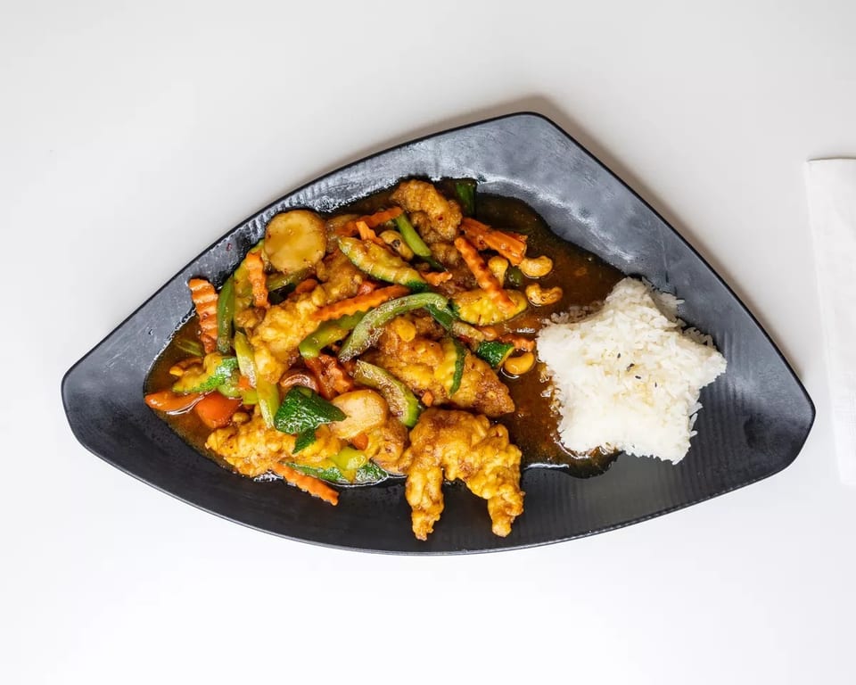 Sweet and sour chicken with mixed vegetables and star-shaped rice on a black plate.
