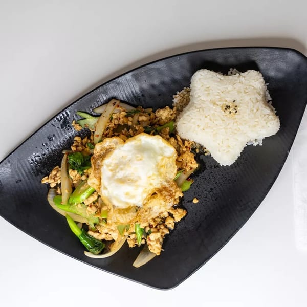Stir-fried chicken and vegetables with a fried egg and star-shaped rice on a black plate.