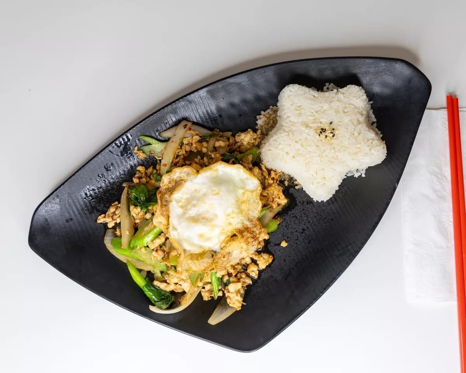 Stir-fried chicken and vegetables with a fried egg and star-shaped rice on a black plate.